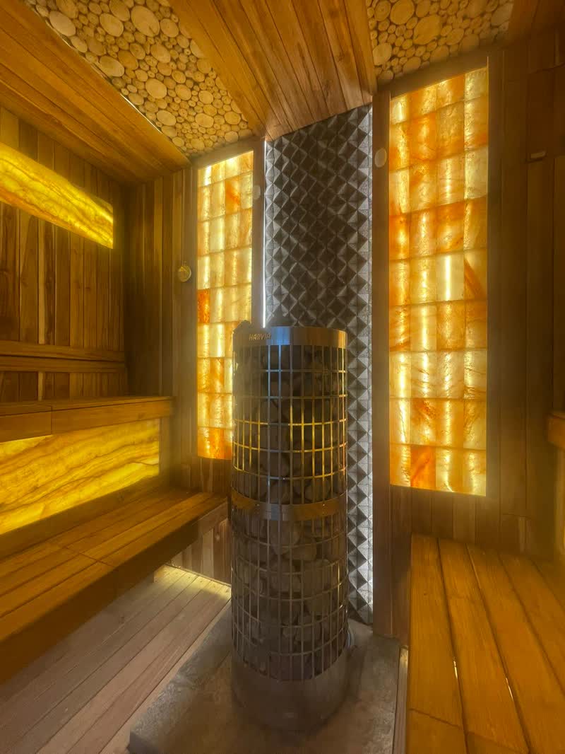 Sauna interior in Bali with backlit onyx panels and a stone heater column
